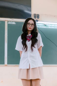 Portrait of a young woman standing in a classroom wearing a school uniform.