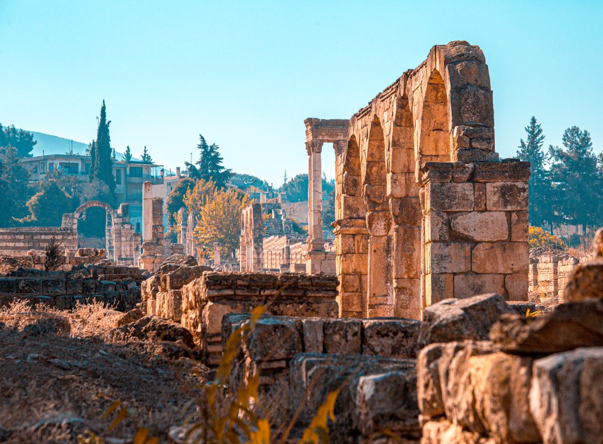 Weathered stone arches and columns of the Baalbek ruins with the modern town visible behind