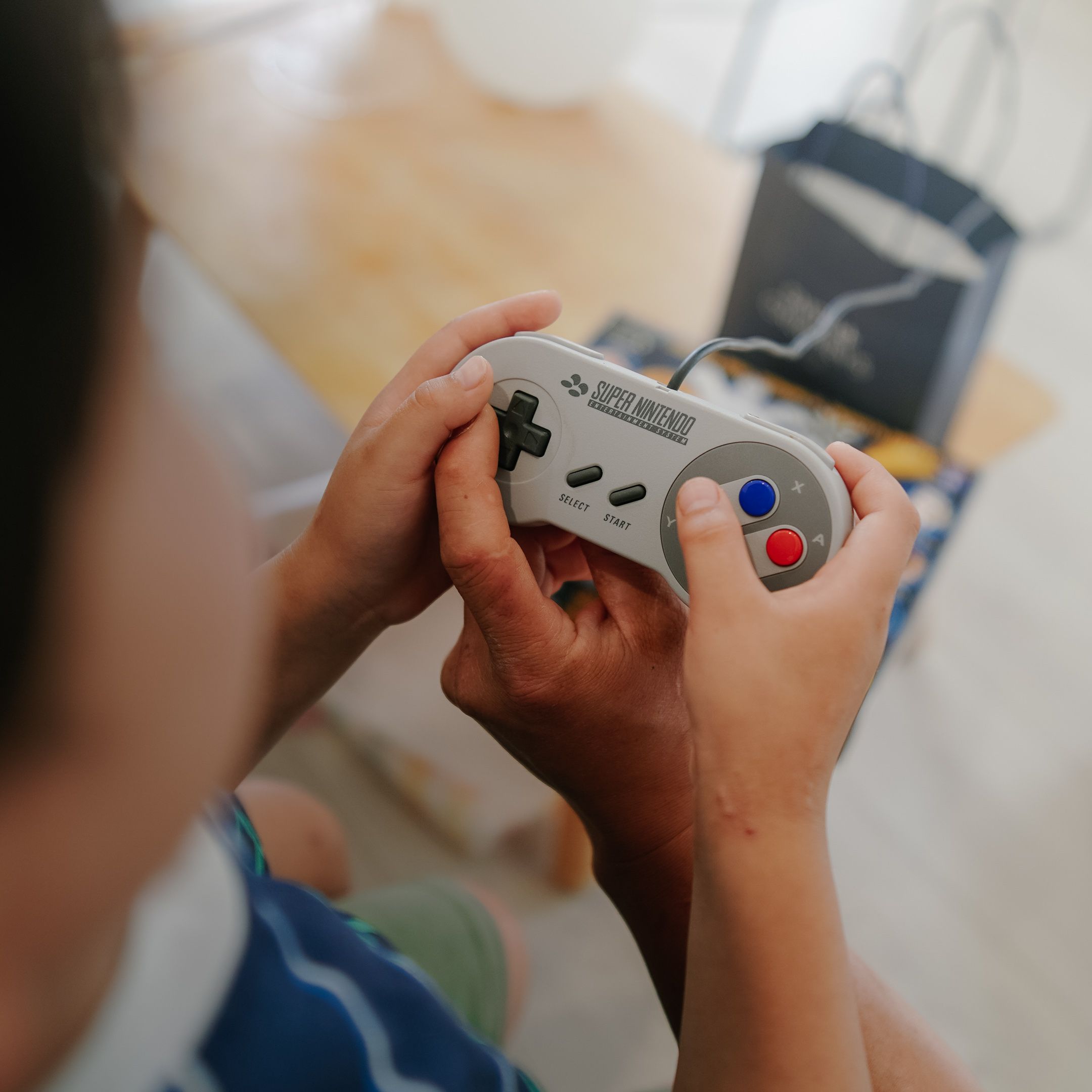 Close-up of two people using a Super Nintendo controller indoors, emphasizing retro gaming.