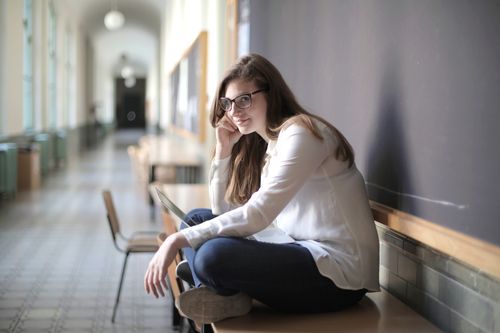 Free A woman in a white shirt and glasses sitting in a hallway. Stock Photo