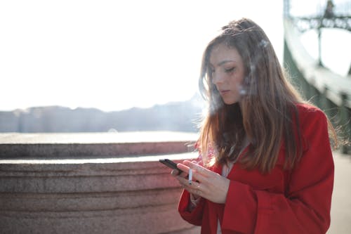 スマートフォンの喫煙を保持している赤いコートの女性