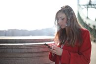 阳光明媚的日子里，一位穿着红色外套的女子在外面抽烟、发短信
