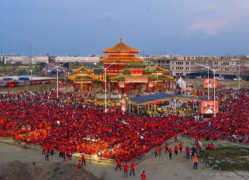 Free A large crowd dressed in red celebrates at a traditional temple festival under a clear sky. Stock Photo