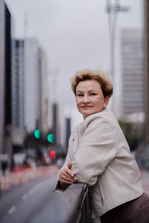 Free Smiling woman in white jacket standing on an urban street with a backdrop of skyscrapers. Stock Photo