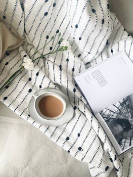 A peaceful setup with coffee, a book, and flowers on a patterned blanket, setting a cozy mood.