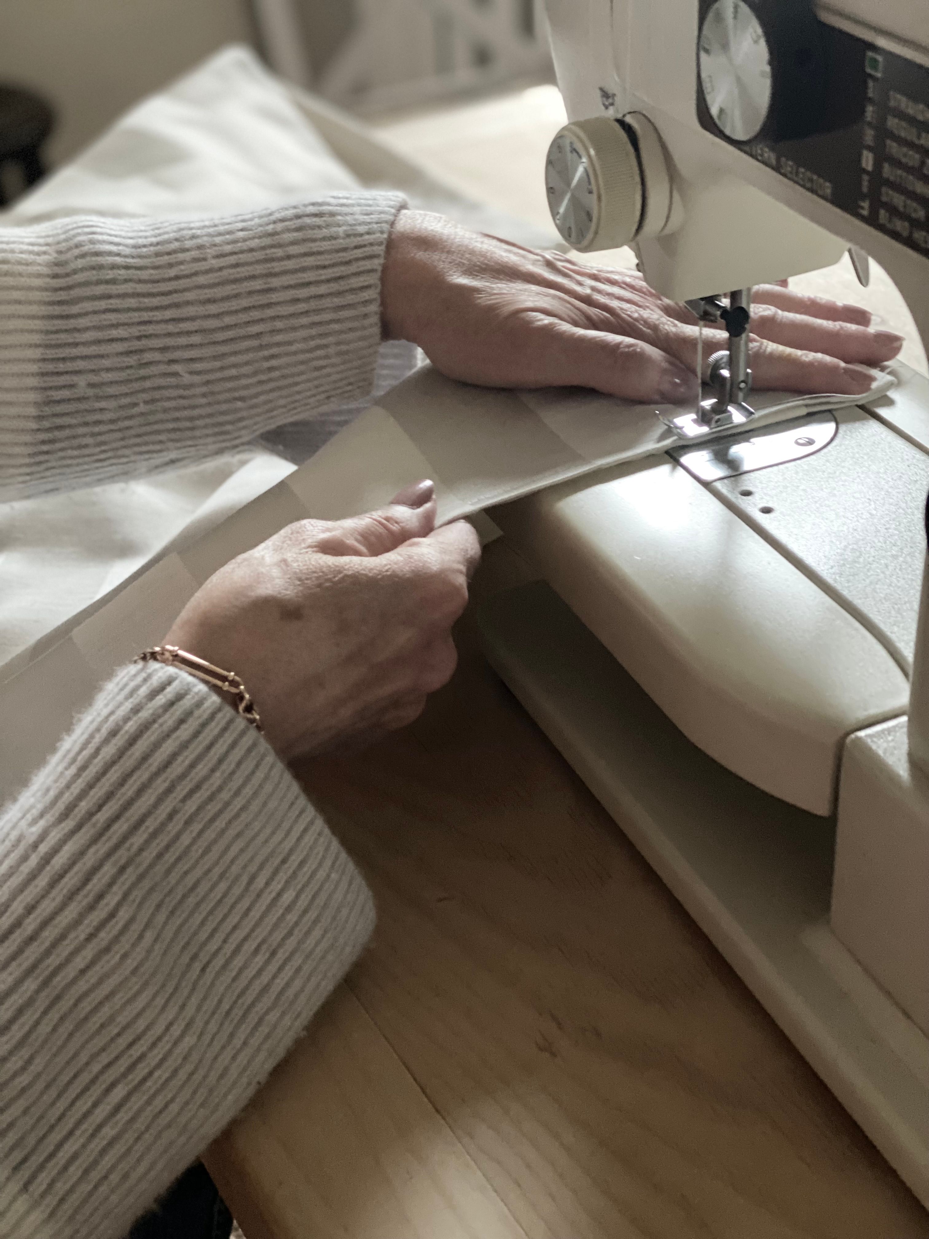 Hands sewing fabric on a machine in a warm, cozy workshop setting.