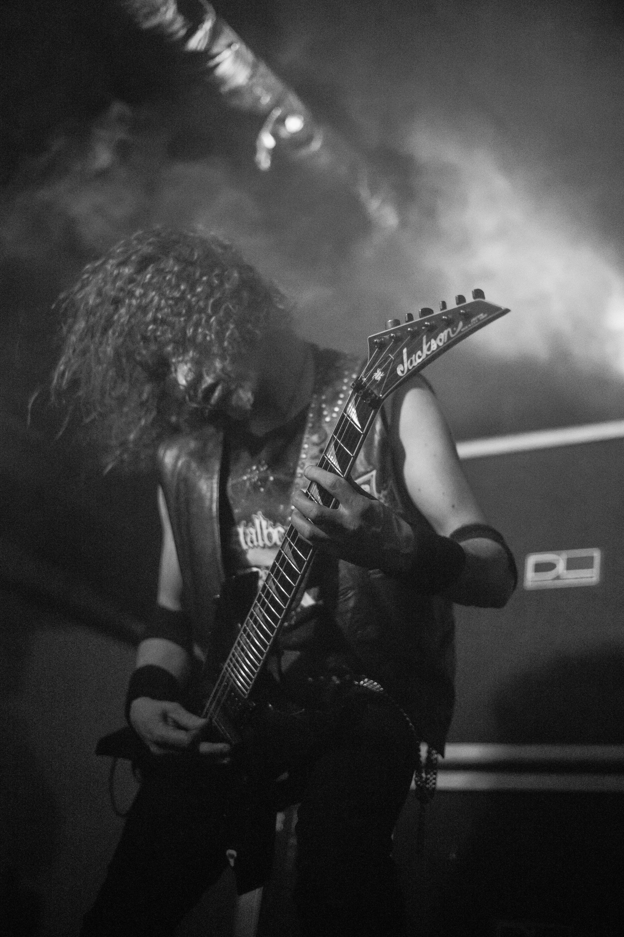 An intense, high-contrast black and white shot of a metal guitarist performing live, capturing the underground scene DISTORTION was designed for