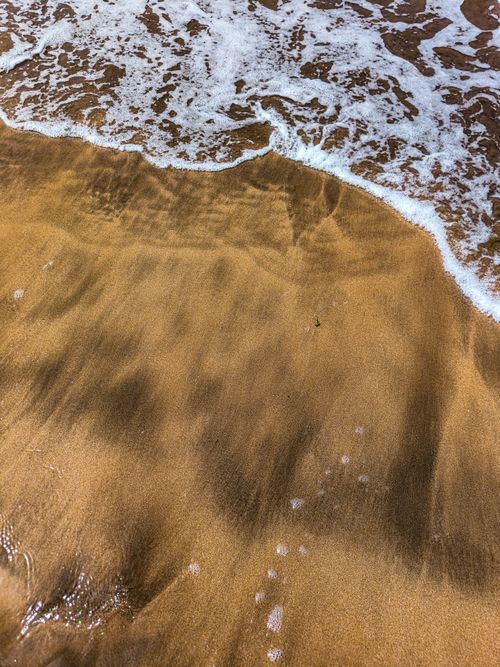 Free Close-up of gentle ocean waves washing over golden sands in Casablanca, Morocco. Stock Photo