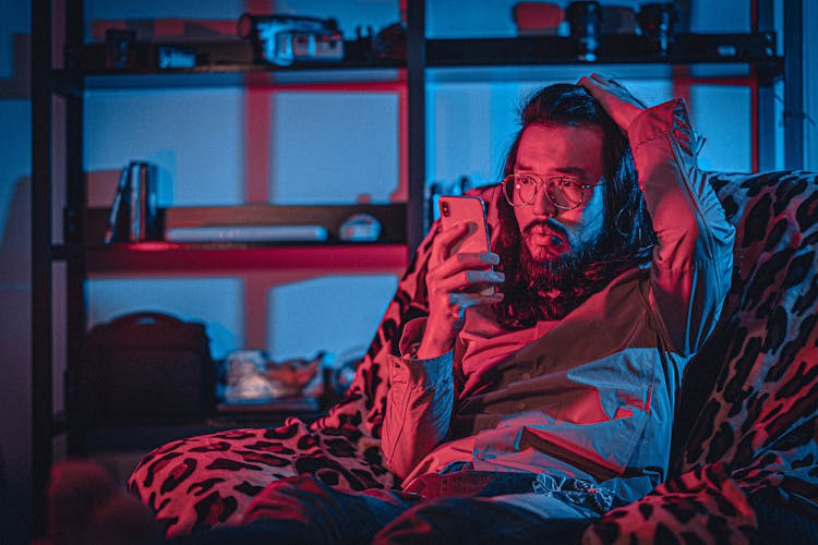 Concerned Ethnic Man Watching Smartphone On Cozy Armchair At Home