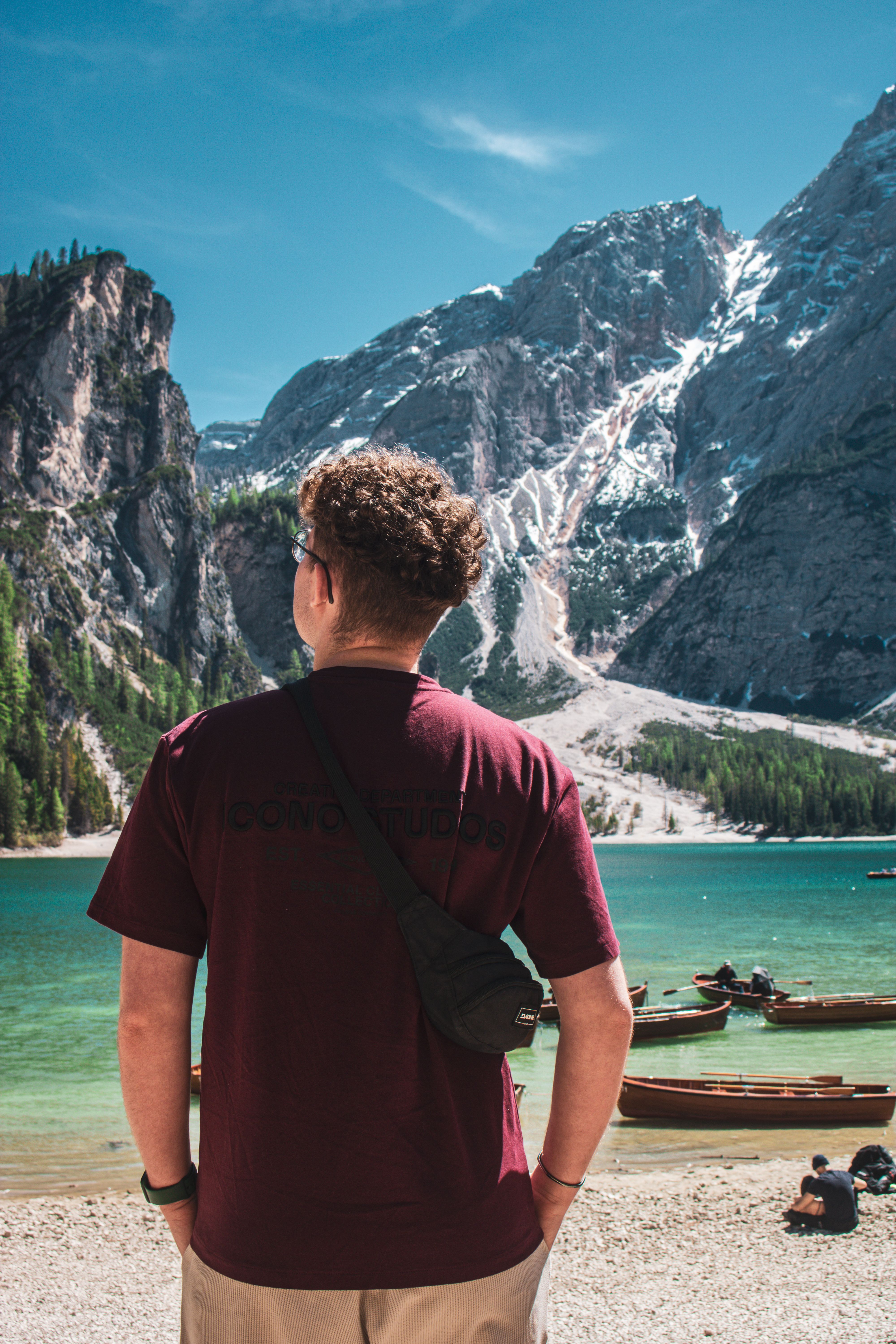 Rear view of a man looking at a serene lake surrounded by towering mountains in Trentino-Südtirol, Italy.