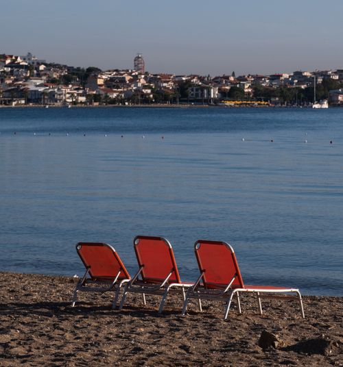 Free Three empty red beach chairs on a sandy shore facing the calm sea in Foça, İzmir. Stock Photo