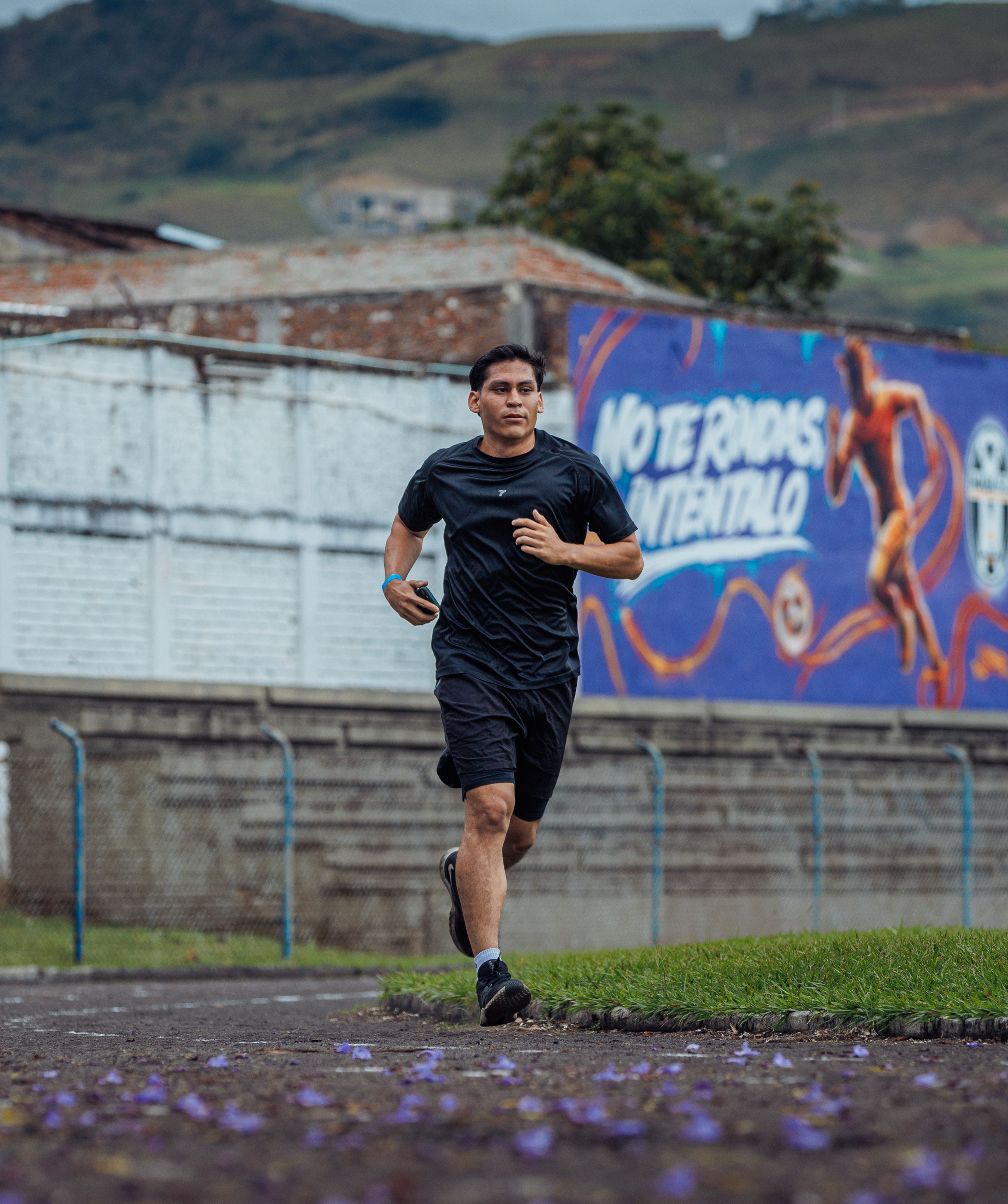 Young man running outdoors in front of a motivational mural in Guadalajara de Buga, Colombia.