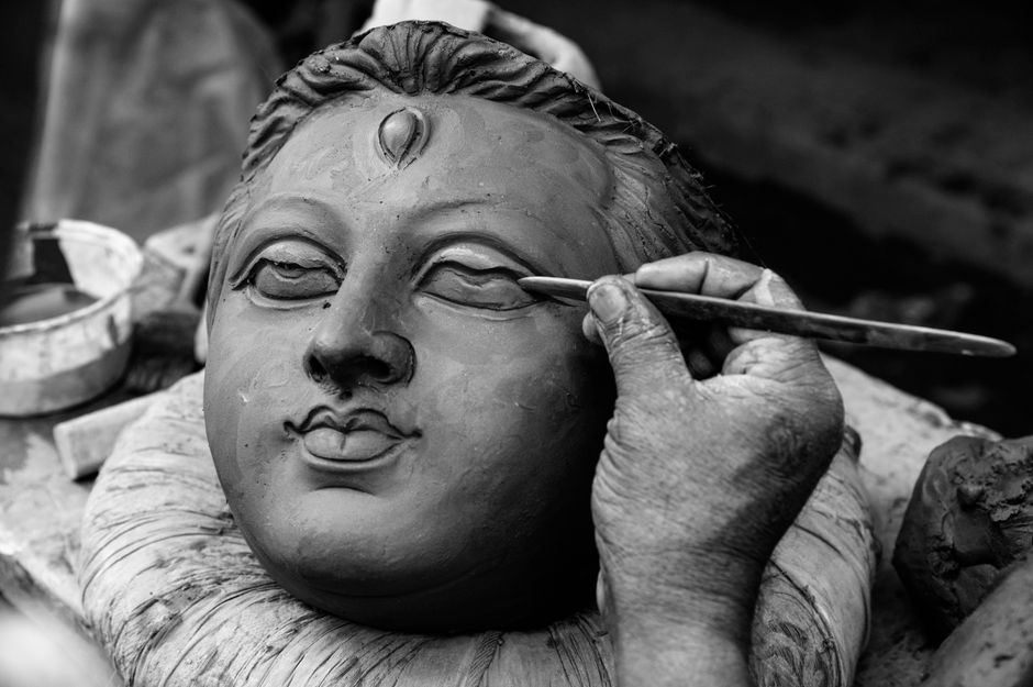 A skilled artisan shapes a clay idol with meticulous detail, highlighting traditional craftsmanship.