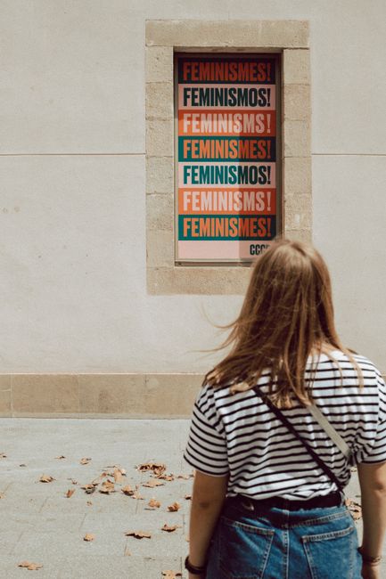Back view of a woman observing a colorful feminism poster on a wall in Barcelona.
