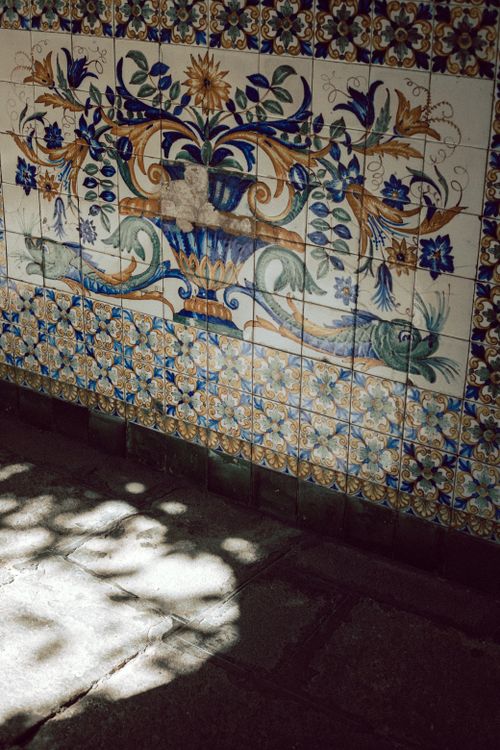 Free Detailed ceramic mosaic tile wall featuring floral patterns and sunlight shadows. Stock Photo