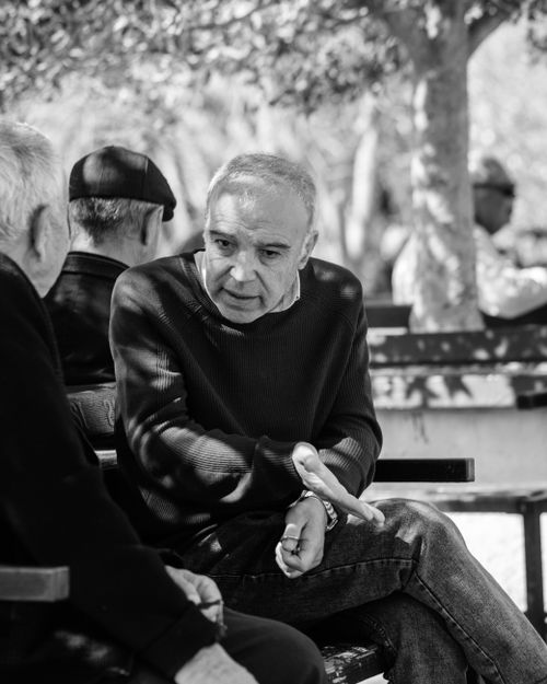 Free Black and white photo of senior adults engaged in conversation on park benches. Stock Photo