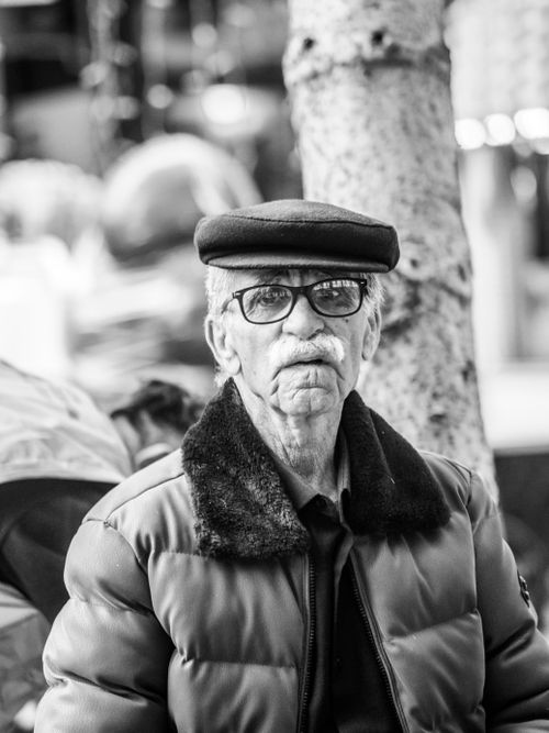 Free Black and white image capturing a senior man with glasses and cap, outdoors. Stock Photo