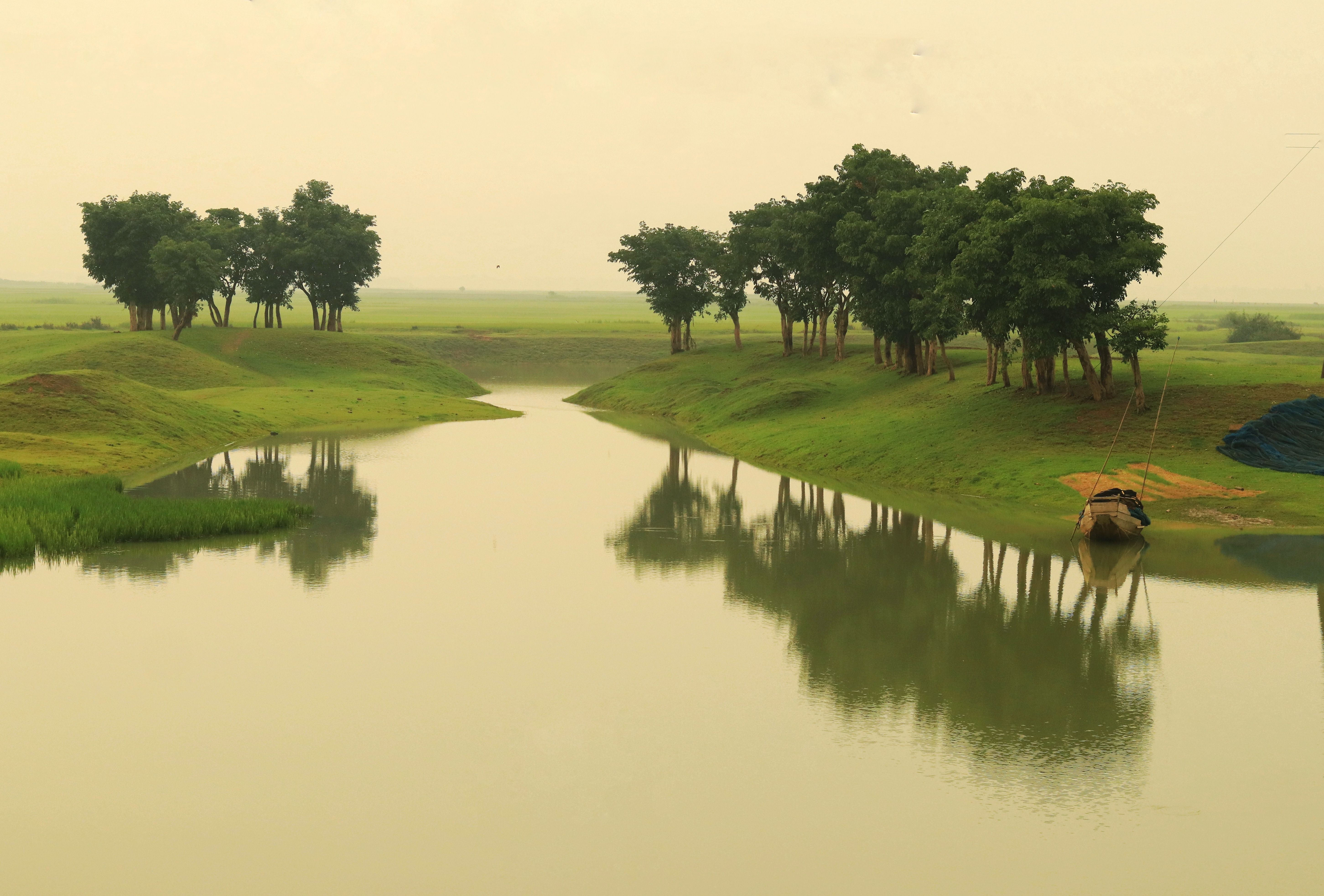 Tranquil river landscape with lush green trees reflecting on the calm water, creating a serene atmosphere.