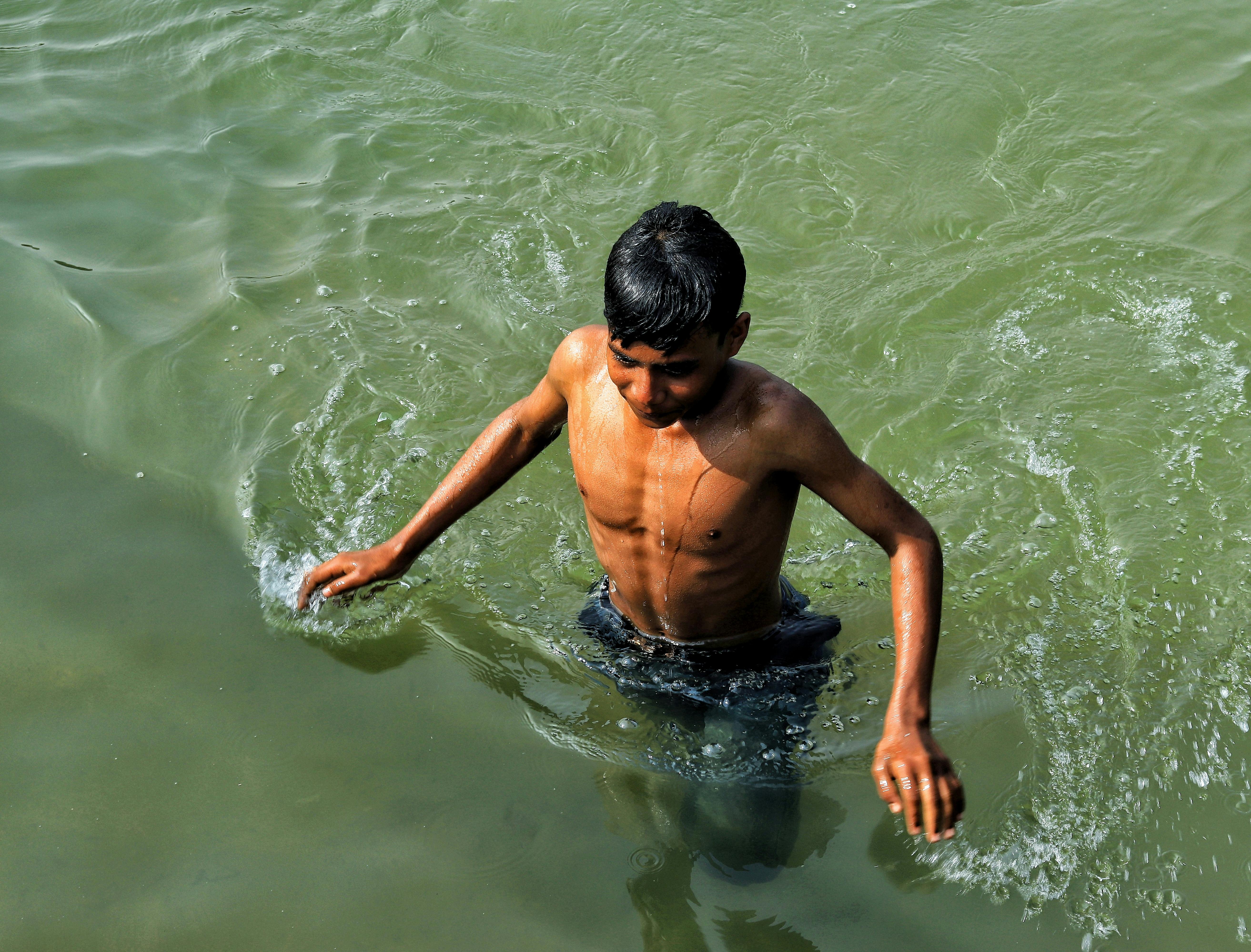 A teenage boy enjoying a swim in a natural water body during a sunny day.