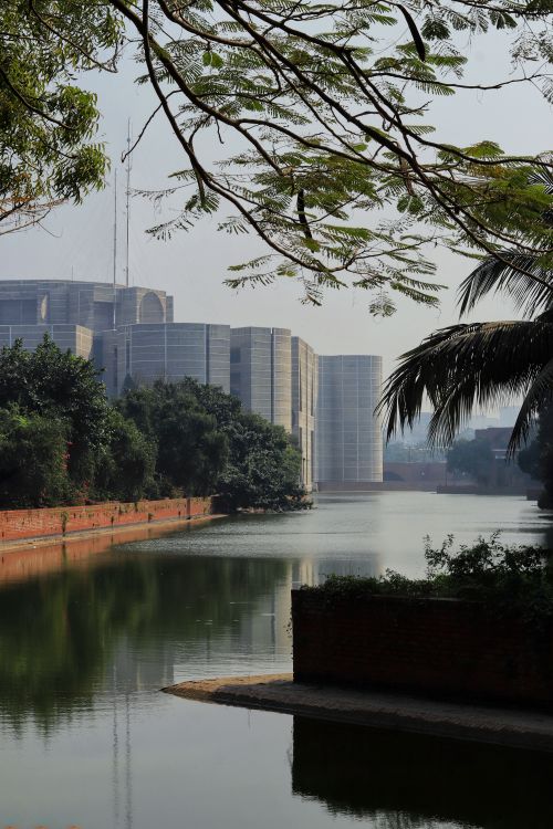 Free Tranquil cityscape featuring modern architecture by a calm waterway, surrounded by lush greenery. Stock Photo