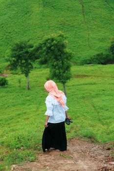 Woman in white and black attire with headscarf walking through a vivid green rural landscape. - Fotografer Sidoarjo