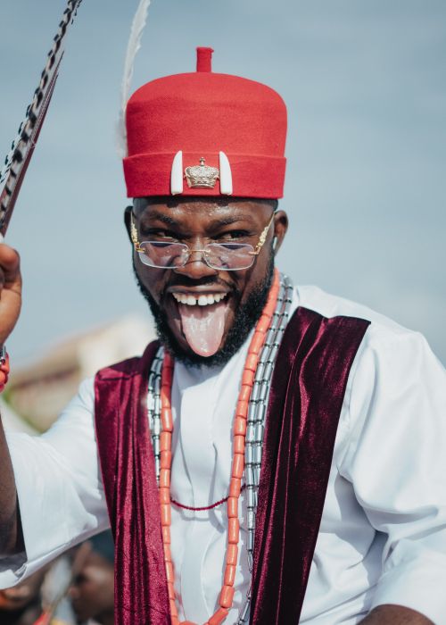 Free A joyful man wearing traditional attire with a red hat and beads celebrates outdoors on a sunny day. Stock Photo