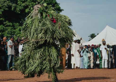 A dancer in a leafy costume performing at an outdoor cultural festival with an audience.