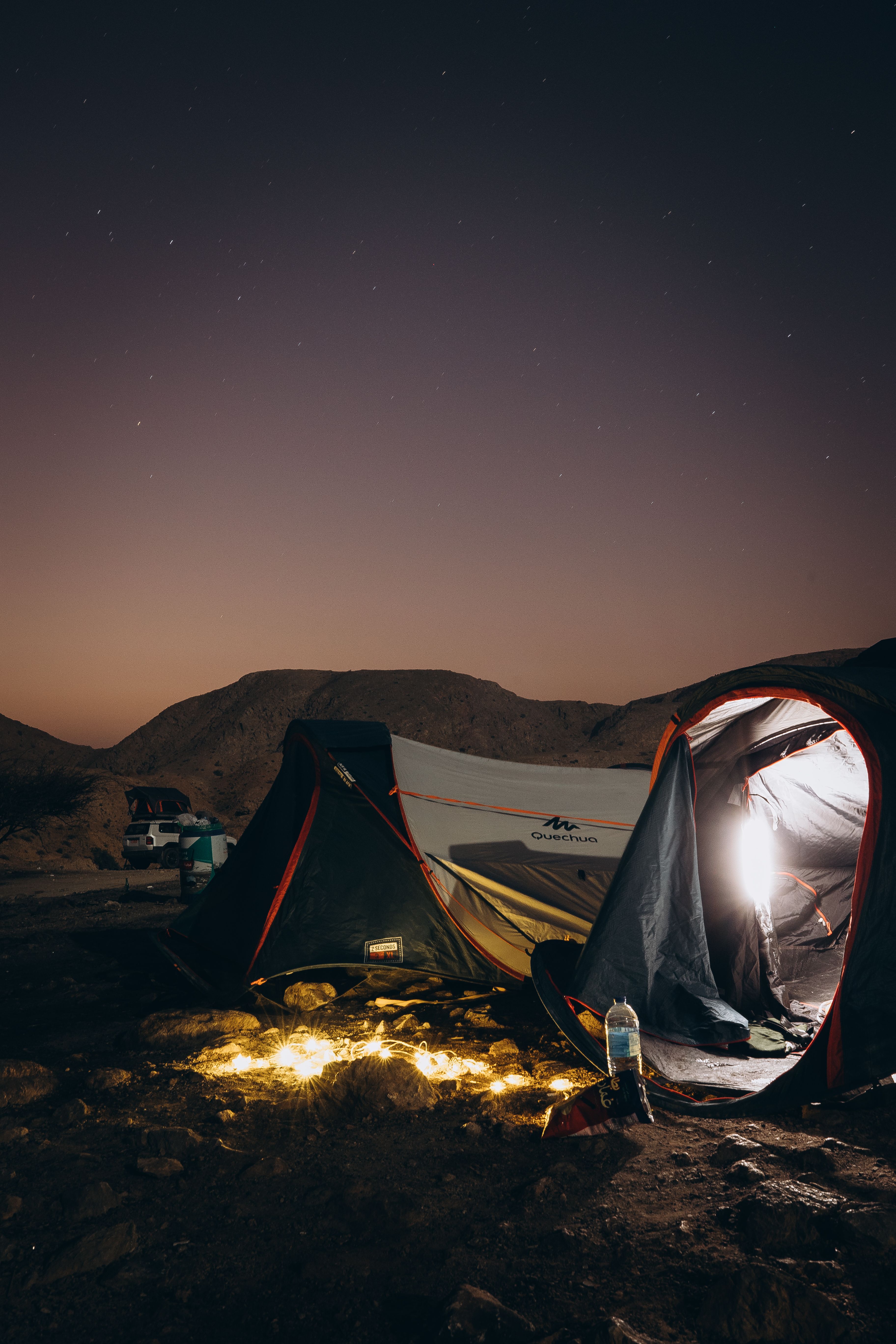 Cozy tent illuminated under a starry night sky in the scenic Omani mountains.