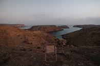 A stunning view of rocky cliffs and a serene bay in Muscat, Oman during twilight with an empty chair in the foreground.