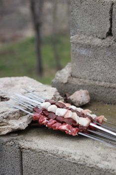 Raw skewered meat placed on a stone surface in an outdoor setting.