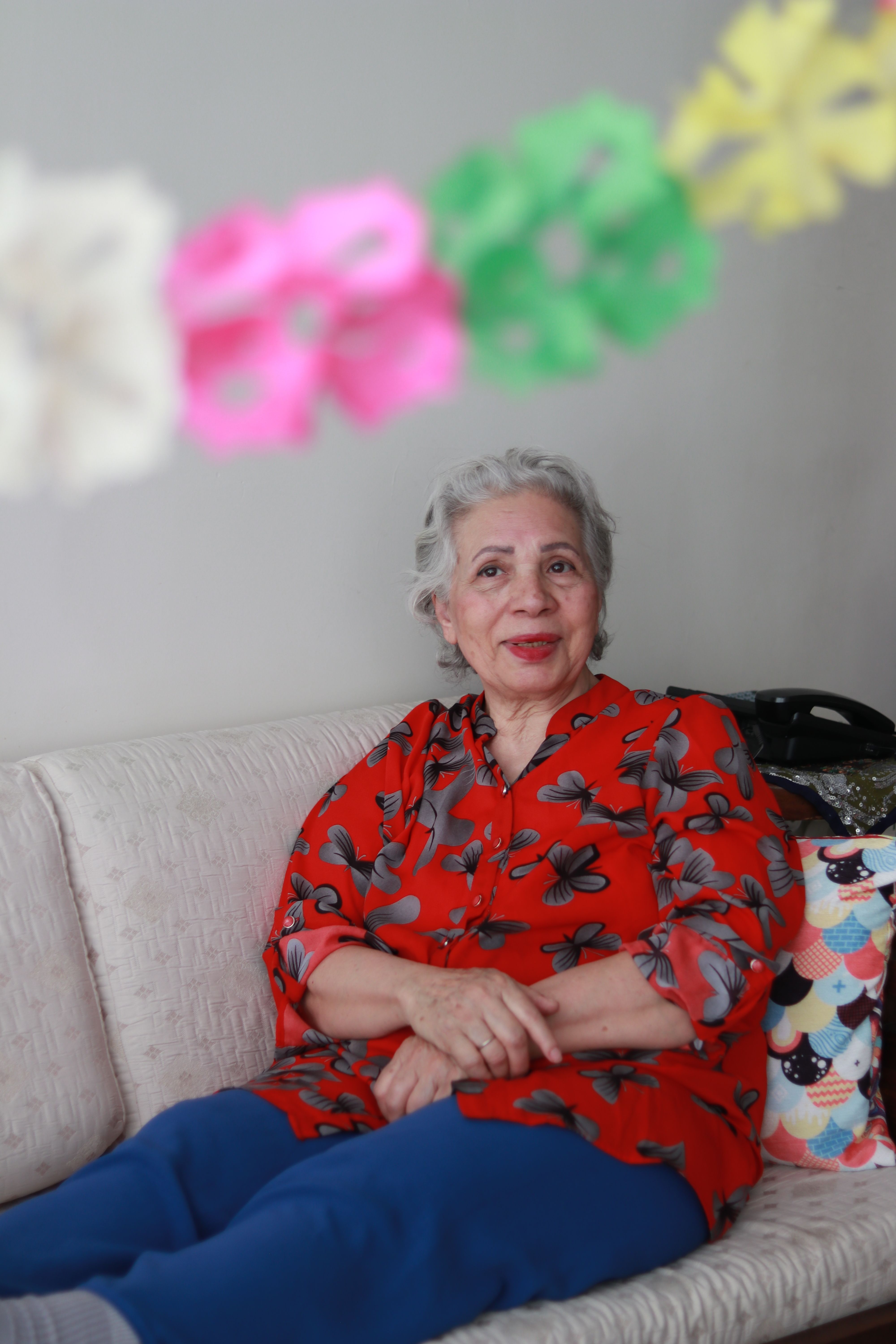 Senior woman seated comfortably indoors surrounded by colorful decorations.