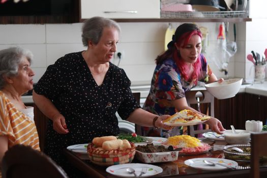 Three women enjoy serving a homemade meal in a lively kitchen setting.