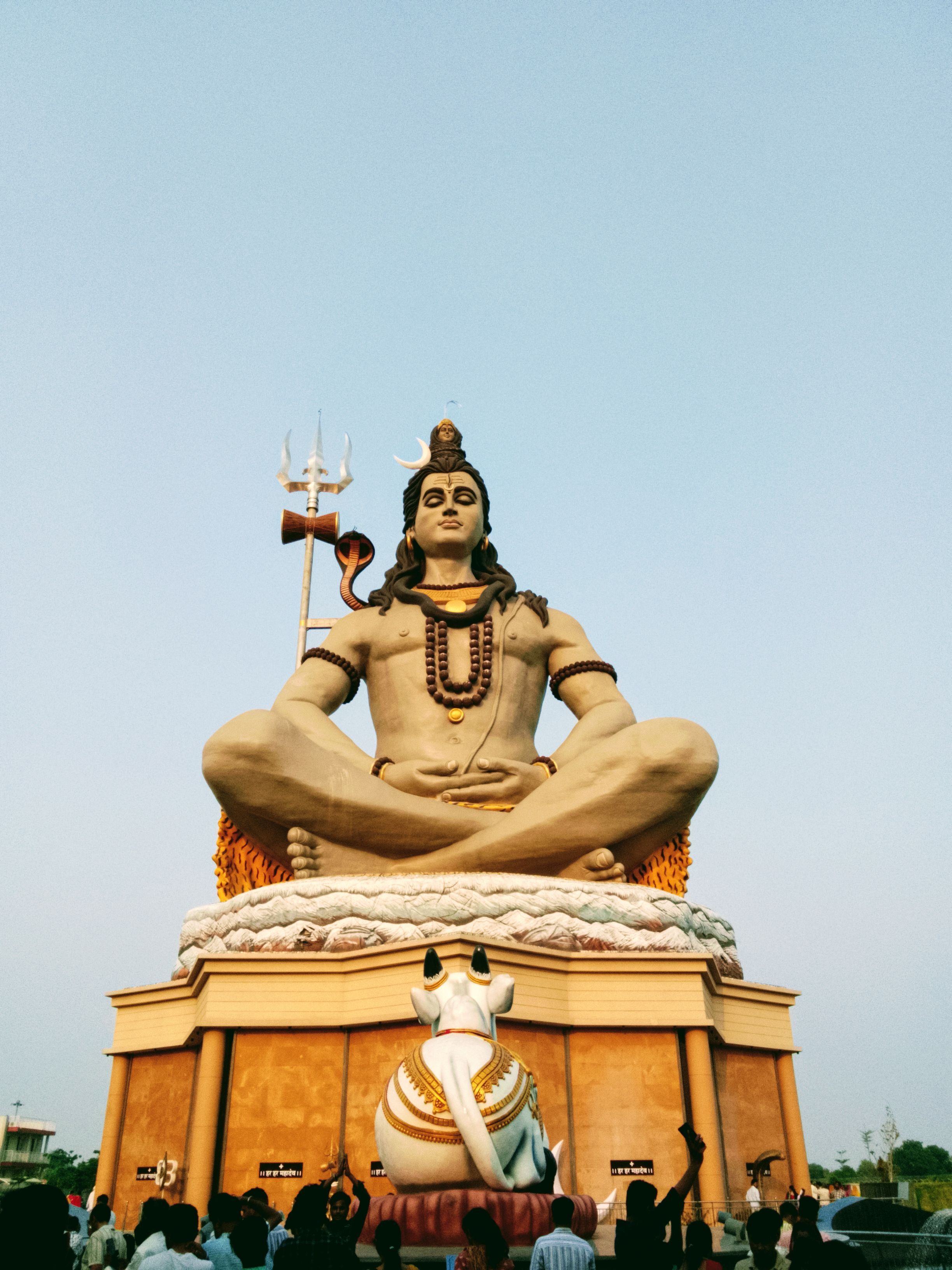 A grand Shiva statue at twilight in Chhatikara, UP, India, attracting visitors.