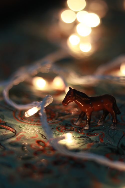 Free A miniature horse toy amid softly glowing fairy lights on a patterned surface. Stock Photo