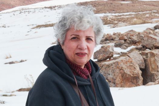 Portrait of a woman standing in a rocky, snowy landscape wearing a dark jacket.
