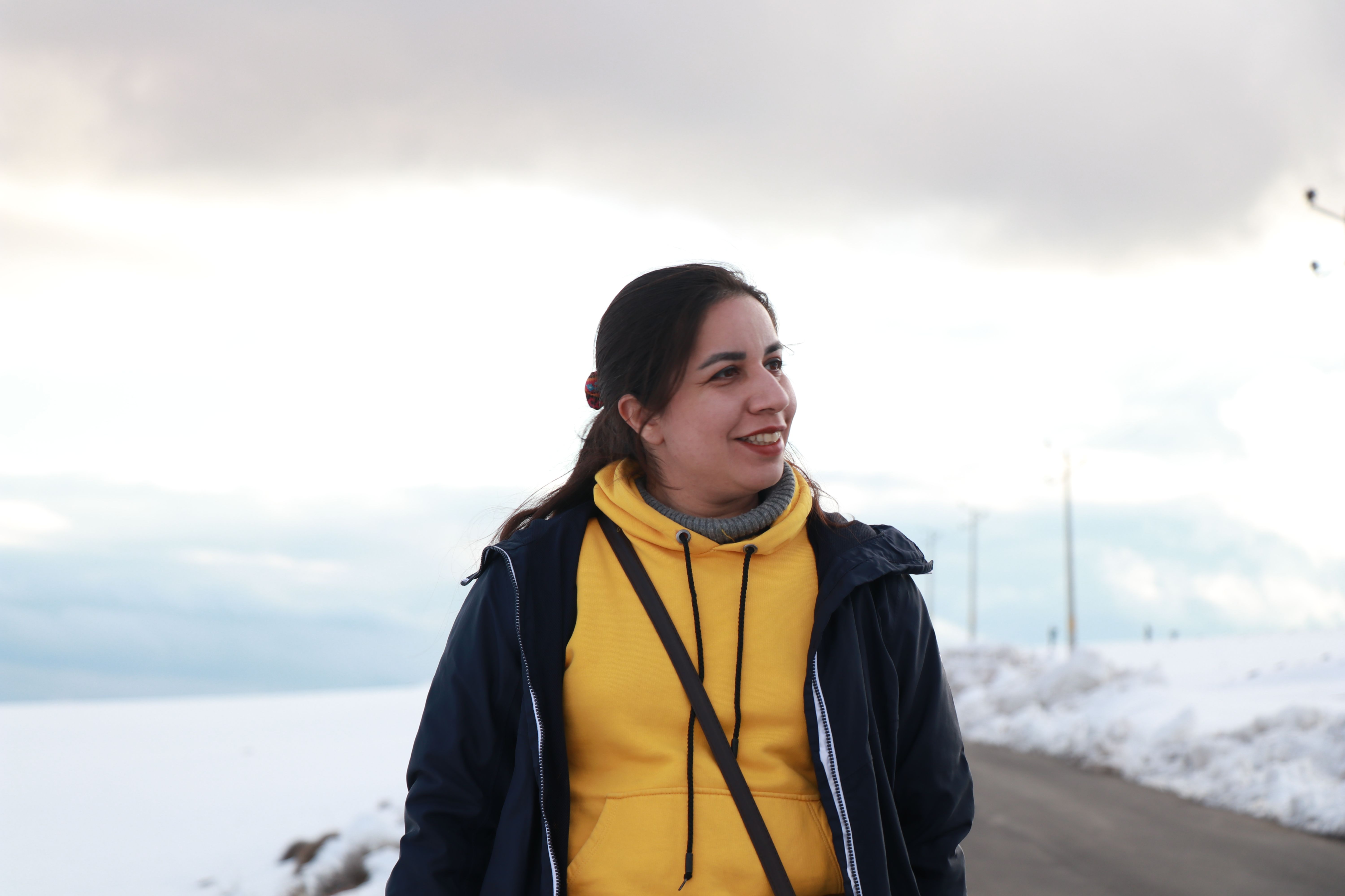 Young woman in a yellow hoodie walking outdoors on a snowy winter day.