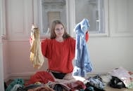 一个穿着红色毛衣的女人正在凌乱的房间里挑选衣服