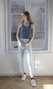 Woman in Blue Tank Top and White Pants Standing Beside Window