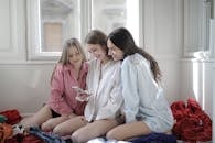 Group of young women browsing smartphone together in messy room
