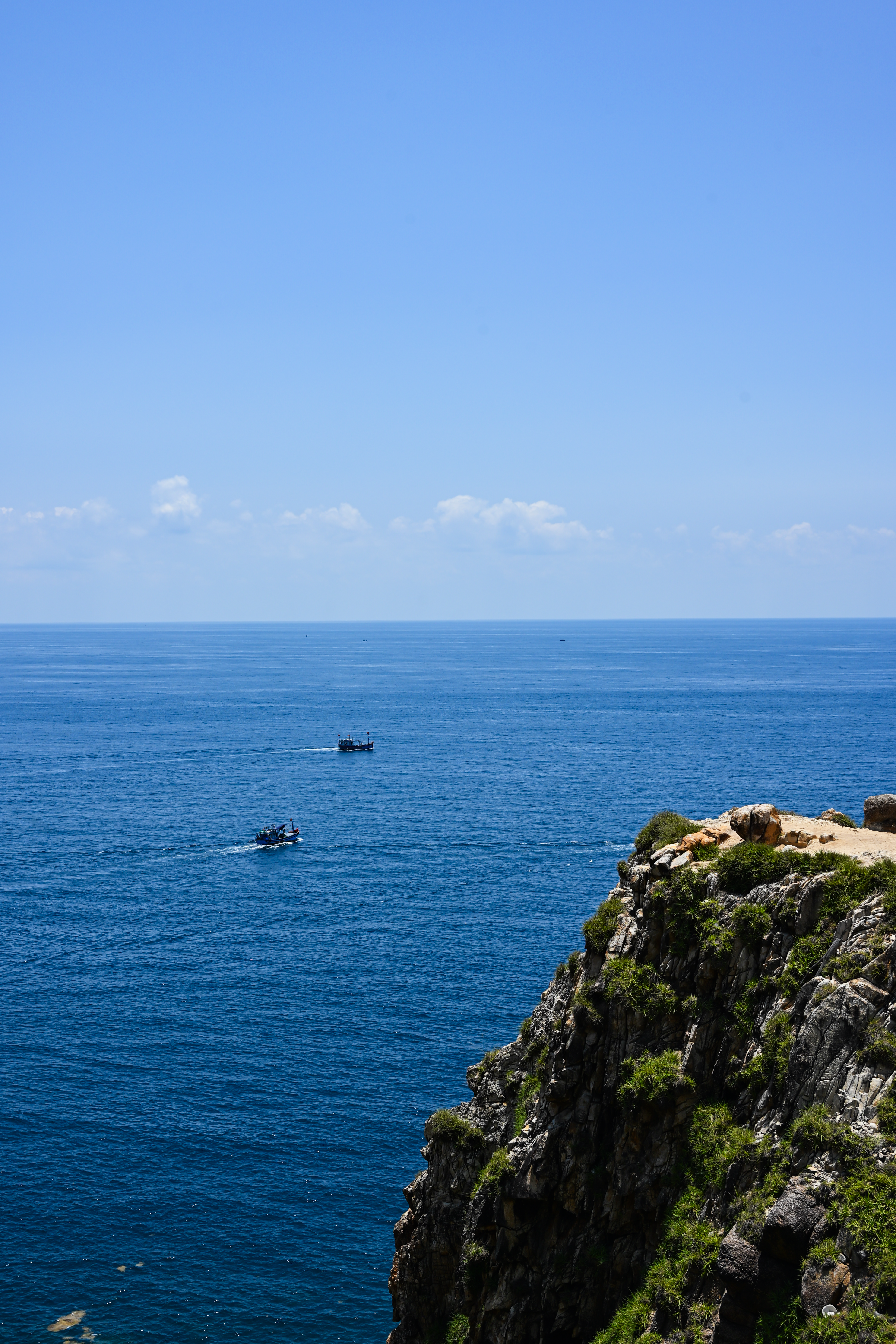 A serene view of boats on the ocean from cliffs in Hòa Xuân, Đắk Lắk, Vietnam.