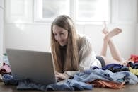 一位快乐的年轻女性穿着衬衫和内裤，躺在凌乱的客厅地板上，衣服散落，一边上网一边在家放松