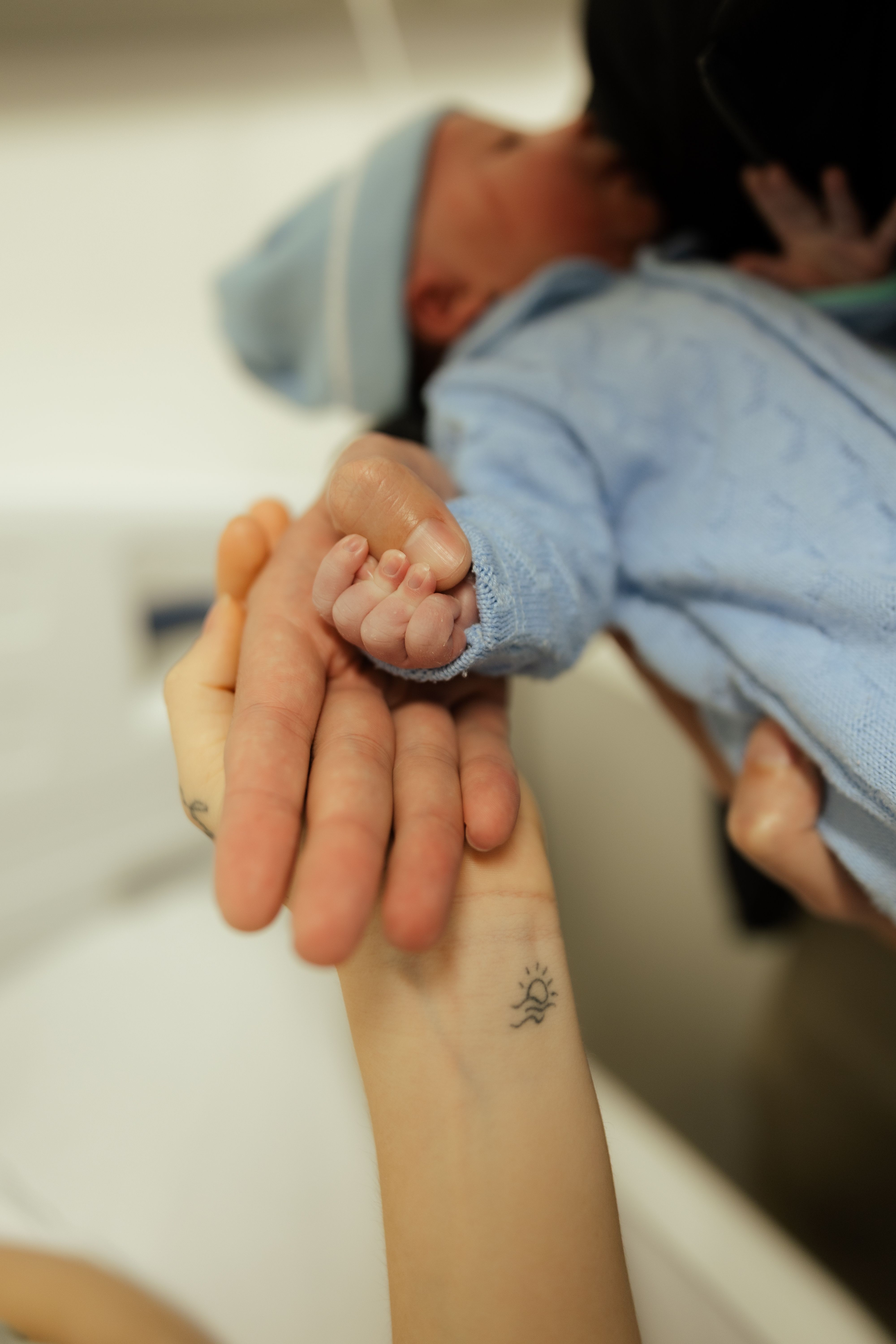 Newborn baby gently holding a parent's hand in a hospital
