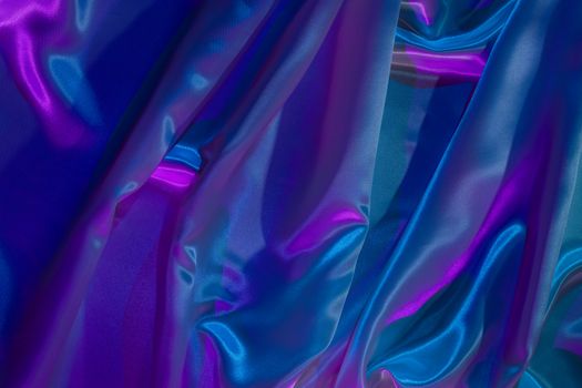 A colorful abstract image of folded satin fabric with neon blue and purple highlights.