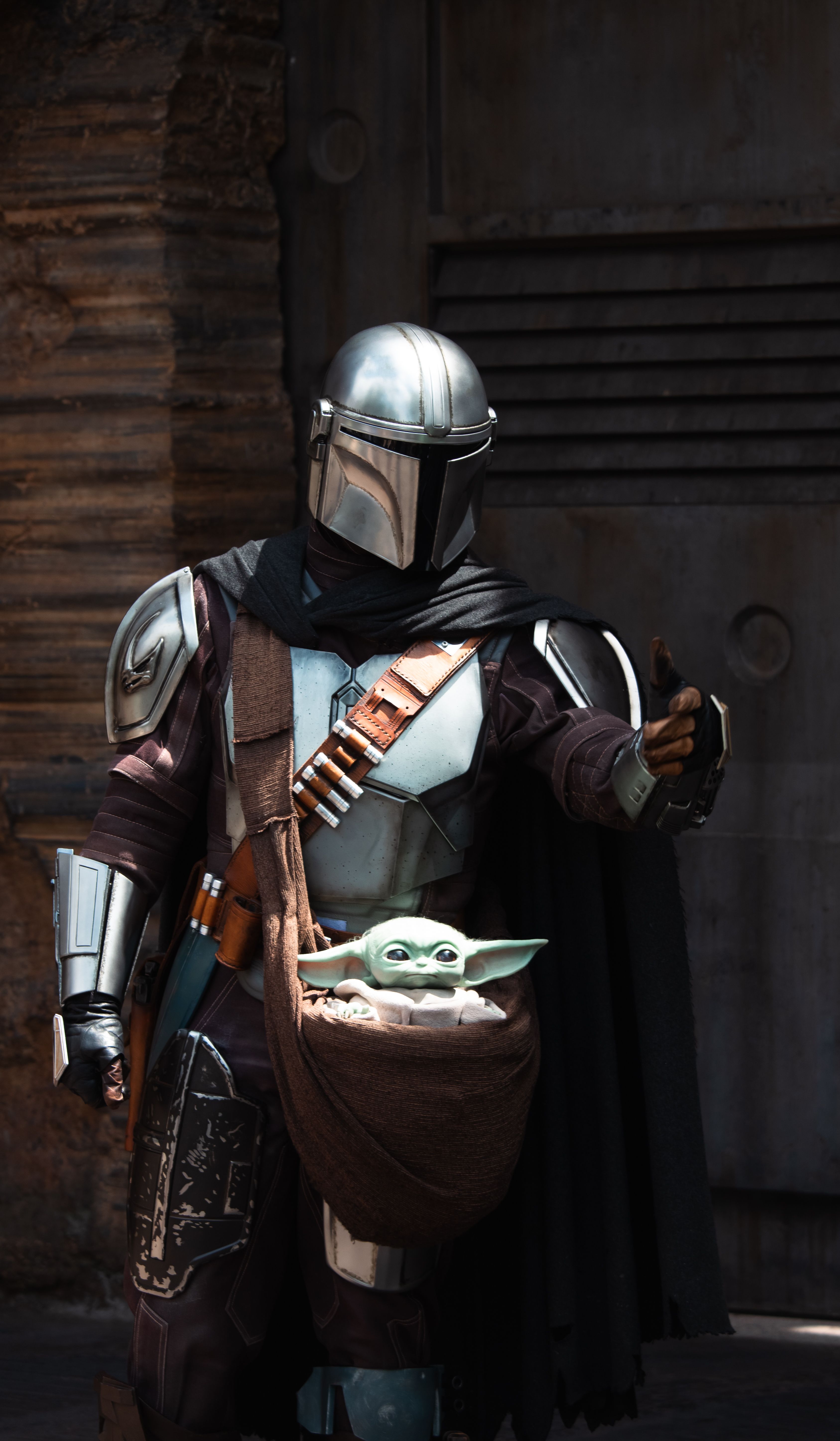 Cosplayer dressed as Mandalorian with Grogu at a Star Wars themed attraction.
