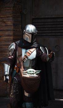 Cosplayer dressed as Mandalorian with Grogu at a Star Wars themed attraction.
