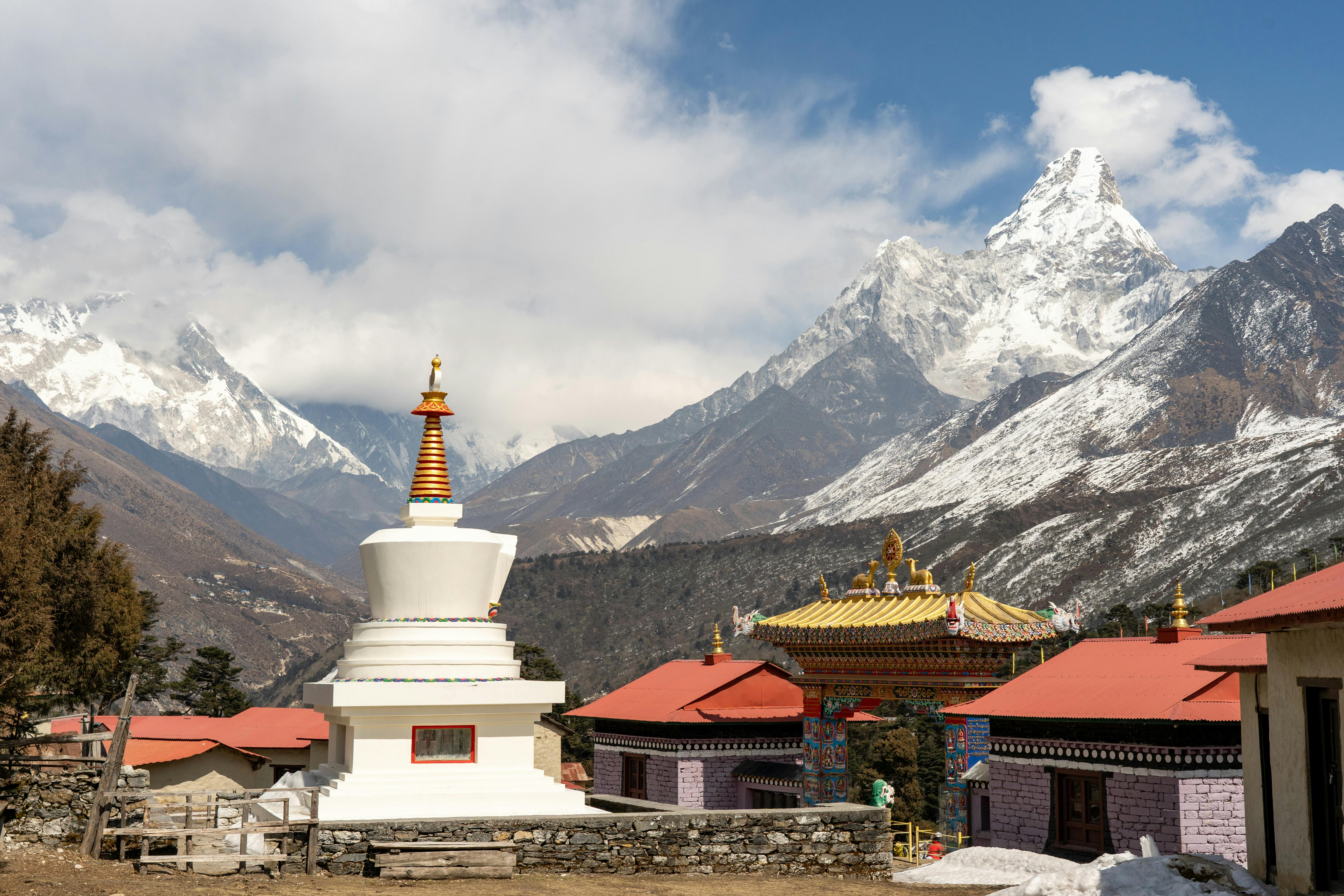 Stupa and traditional buildings with Himalayan mountains in background, showcasing serene beauty.
