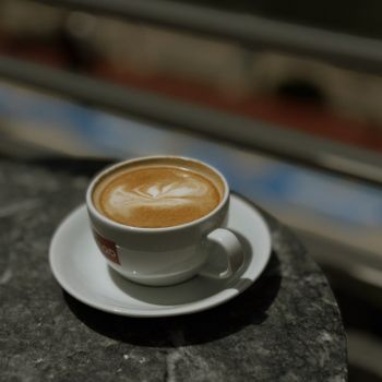 Cappuccino topped with heart-shaped latte art served on a dark marble table outdoors.