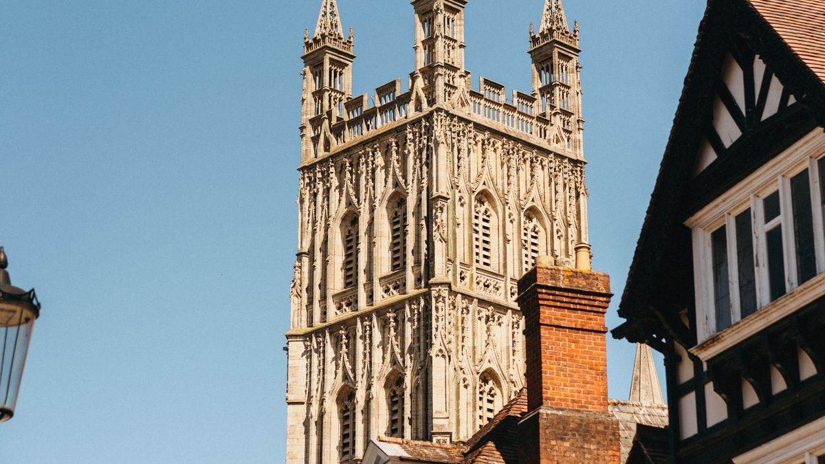 Gloucester Cathedral tower seen beside a timber-framed building on a sunny day