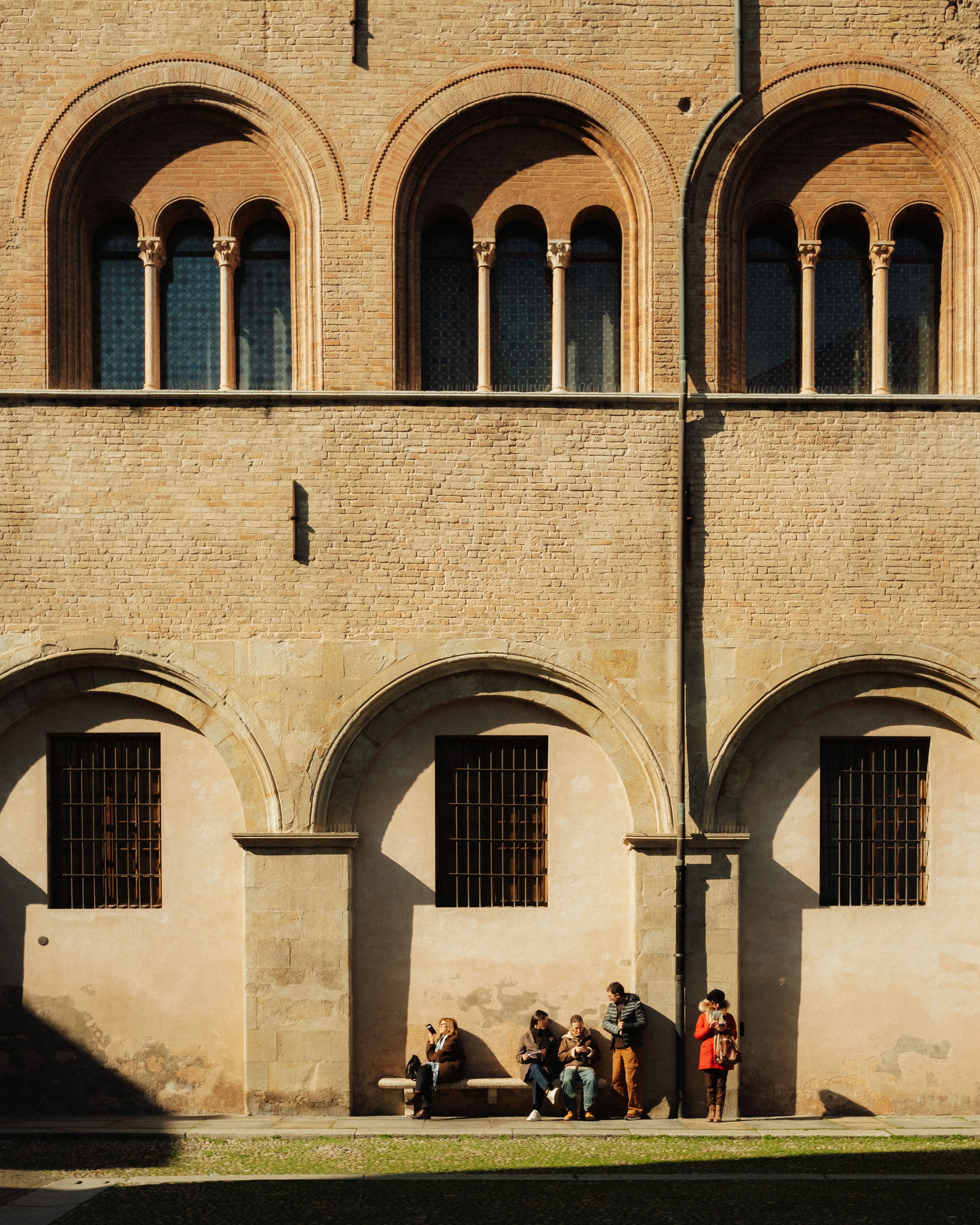 A historic building facade in Parma, Italy, with tourists relaxing and enjoying the scene.