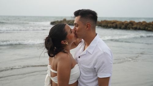 Free A couple shares a romantic kiss by the ocean shore, embodying love and connection. Stock Photo